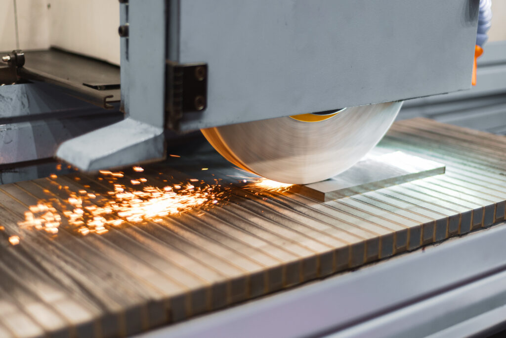 An industrial grinding machine in operation, with a spinning wheel sending sparks flying as it processes a flat metal piece, representing assets covered by industrial equipment financing.