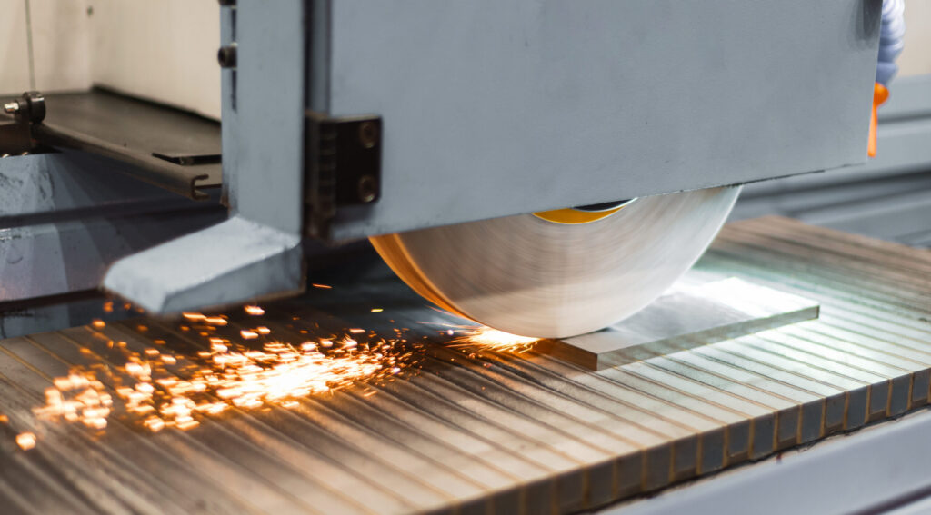 An industrial grinding machine in operation, with a spinning wheel sending sparks flying as it processes a flat metal piece, representing assets covered by industrial equipment financing.